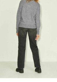 Grauer Strickpullover mit rundem Halsausschnitt, kombiniert mit dunkelblauen Jeans. Das Outfit hat eine lockere Passform und schwarze klobige Stiefel.