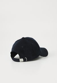 Casquette en velours côtelé bleu marine foncé, avec une visière incurvée, un tissu texturé et une sangle ajustable à l'arrière avec une boucle en métal argenté.