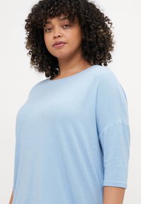 Light blue, short-sleeve top made from soft fabric, featuring a rounded neckline and loose fit, with smooth texture and relaxed silhouette.