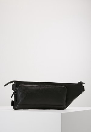 Bolsa de cintura de cuero negro con bolsillo delantero con cremallera y correa ajustable, presentada sobre una superficie blanca con un fondo claro.
