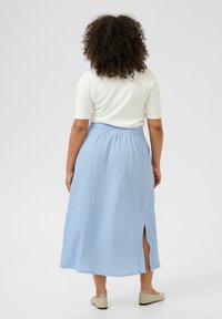 Light blue, crinkled fabric maxi skirt with an elastic waistband and side slit. Paired with a white fitted top and beige slip-on shoes.