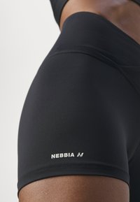 Pantaloni corti neri alla vita alta realizzati in tessuto liscio con il logo NEBBIA bianco sull'orlo inferiore. Presentano un design senza cuciture per garantire comfort.