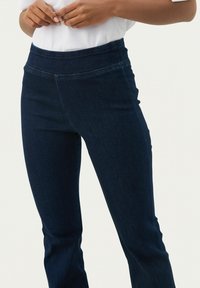 Donkerblauwe denim broek met een nauwsluitende tailleband, met een gladde textuur en subtiele stikseldetails, ontworpen voor een aansluitende fit.