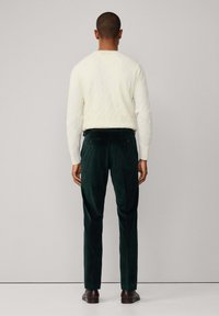 Zelené kordové nohavice v kombinácii s bielym sveterom z pleteniny, z pohľadu zozadu. Výrazné prvky zahŕňajú dve zadné vrecká a textúrovanú tkaninu.