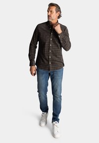 Bruin geruit overhemd met knopen, gemaakt van katoen, met lange mouwen en een kraag, gecombineerd met blauwe jeans en witte sneakers.