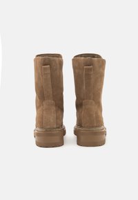 Botas de tobillo de ante marrón con punta redondeada, suela de goma plana y tirador trasero. Textura suave con acentos cosidos y diseño duradero.