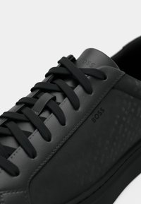 Baskets noires avec une tige en cuir lisse, des accents texturés, des lacets proéminents et la marque "BOSS" sur la languette et le côté.