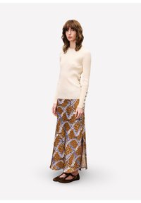 Haut à manches longues côtelé crème avec accents en boutons, assorti à une jupe maxi marron à motifs avec des motifs bleu et beige, portée avec des ballerines noires.