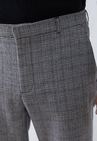 Pantalons à carreaux gris en tissu tissé, présentant un motif à carreaux subtil, une texture lisse et des poches avant avec des éléments de design classiques.