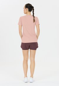 Ljusrosa kortärmad skjorta matchad med vinröda shorts, visad på en person som står med ryggen mot kameran. Slät tyg, avslappnad passform, vita sneakers.