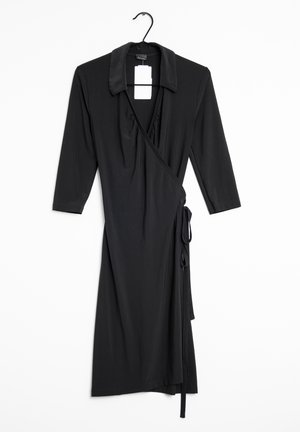 Vestido negro envolvente con mangas de tres cuartos, cuello con solapa, detalle de lazo en la cintura y tejido fruncido en el busto. Tela suave y elástica.