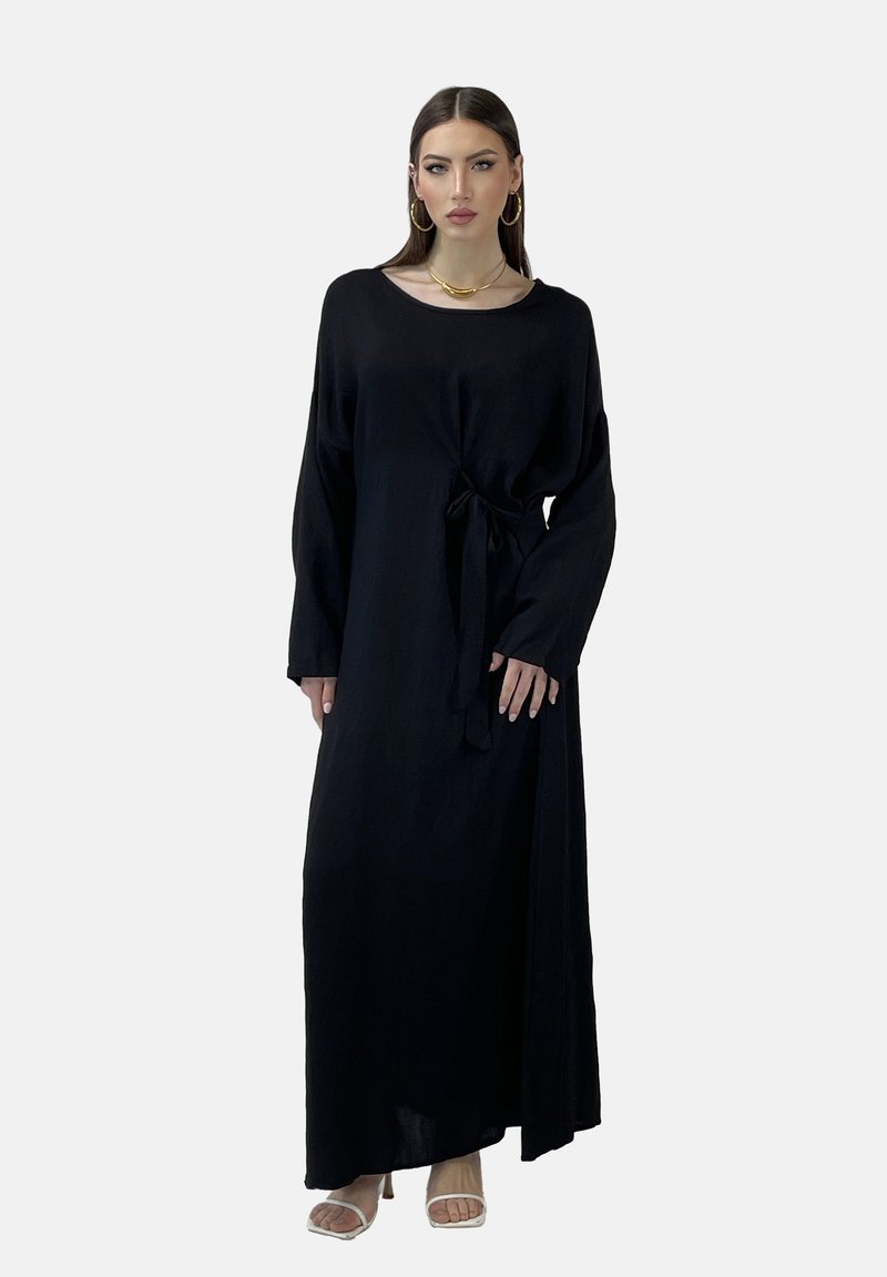 Zwarte maxibedrijf met lange mouwen en een strik taille, losse pasvorm en een zachte textuur. Het model draagt een paar sandalen met banden, wat de soepele draping en flow laat zien.