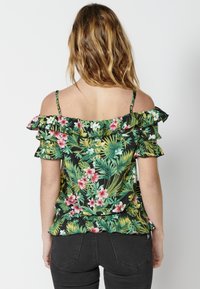 Top off-the-shoulder in tessuto nero con stampa floreale colorata, maniche arricciate e silhouette aderente con orlo a peplo.