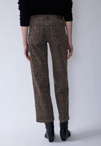 Kalhoty se vzorem leopardí kůže v hnědé a černé barvě, s pouzdrovým střihem, pěti kapsami a hladkou texturou. Černé kotníkové boty doplňují vzhled.
