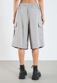 Shorts cargo gris clair avec une taille élastique, deux poches latérales et une poche arrière, présentant une coupe ample et des poignets ourlés.