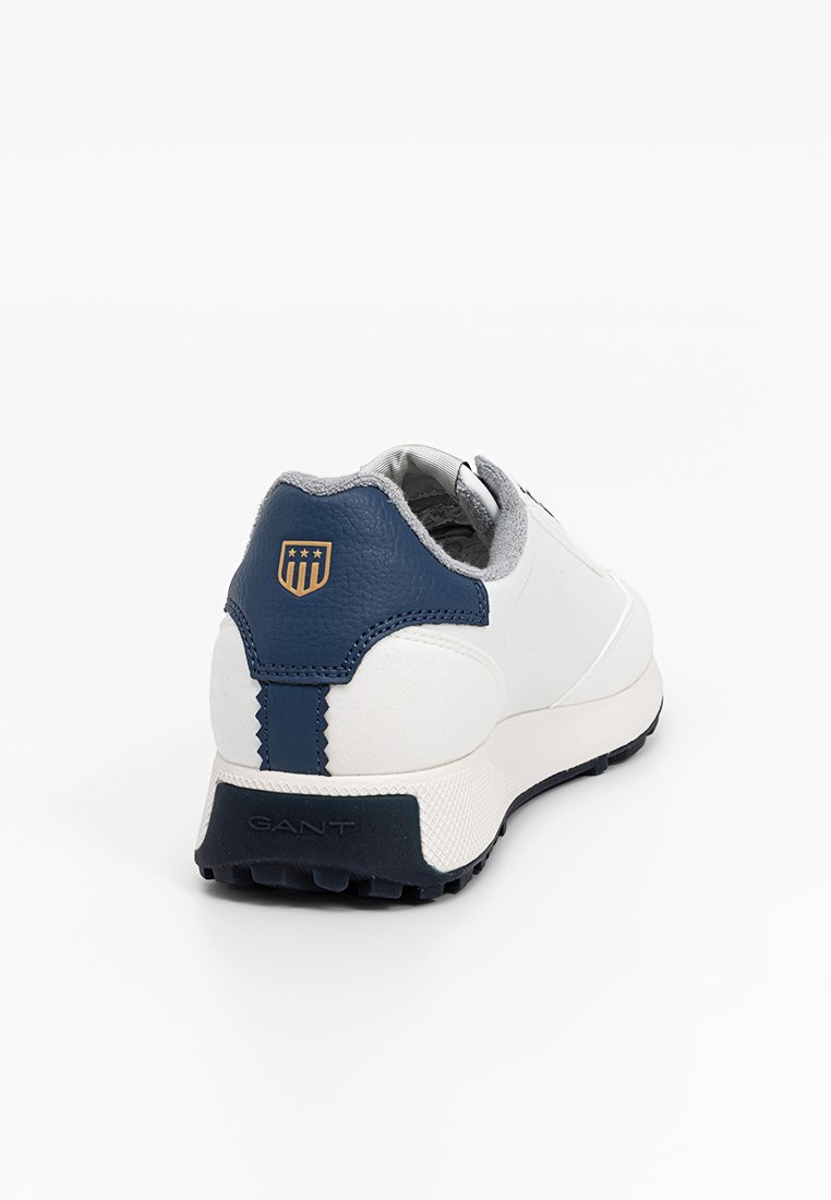 Sneaker bianco con accenti navy, dotato di un retro testurizzato, materiale superiore liscio e un dettaglio logo vicino al tallone. Suola in gomma.