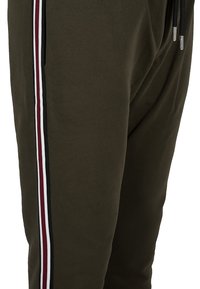Olivově zelené tepláky slim fit, s bílými, černými a vínovými vertikálními pruhy na bocích a elastickým pasem.