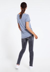 Camiseta a rayas azul y blanca, de manga corta, corte relajado. Combinada con jeans ajustados gris oscuro y zapatillas blancas. Fondo liso.
