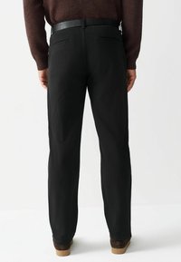 Fekete, egyenes szabású nadrág, két hátsó zsebbel és sima textúrával. Sötét övvel és barna cipővel viselve.