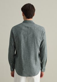 Camicia grigia in flanella con una sottile trama melange, polsini con bottone e orlo arrotondato. Presenta un collo classico e un dettaglio nella yoke sul retro.