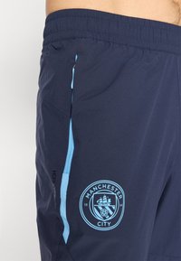 Mørkeblå shorts med lyseblå detaljer, elastisk talje og sidelommer. Fremhæver et rundt Manchester City-logo på låret.