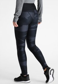 Musta leggingit, joissa on teksturoitu kuvio, johon kuuluu viistoja ja raidoitettuja muotoja. Korkea vyötärö tukee. Yhdistetty mustiin urheilukenkiin.