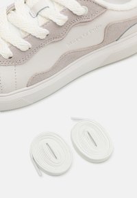 Heledhall hall sneakers, mille kreemjat sametist detaile, paksude, tekstureeritud valgete paeltega. Kaasas on kaks täiendavat valget paela.