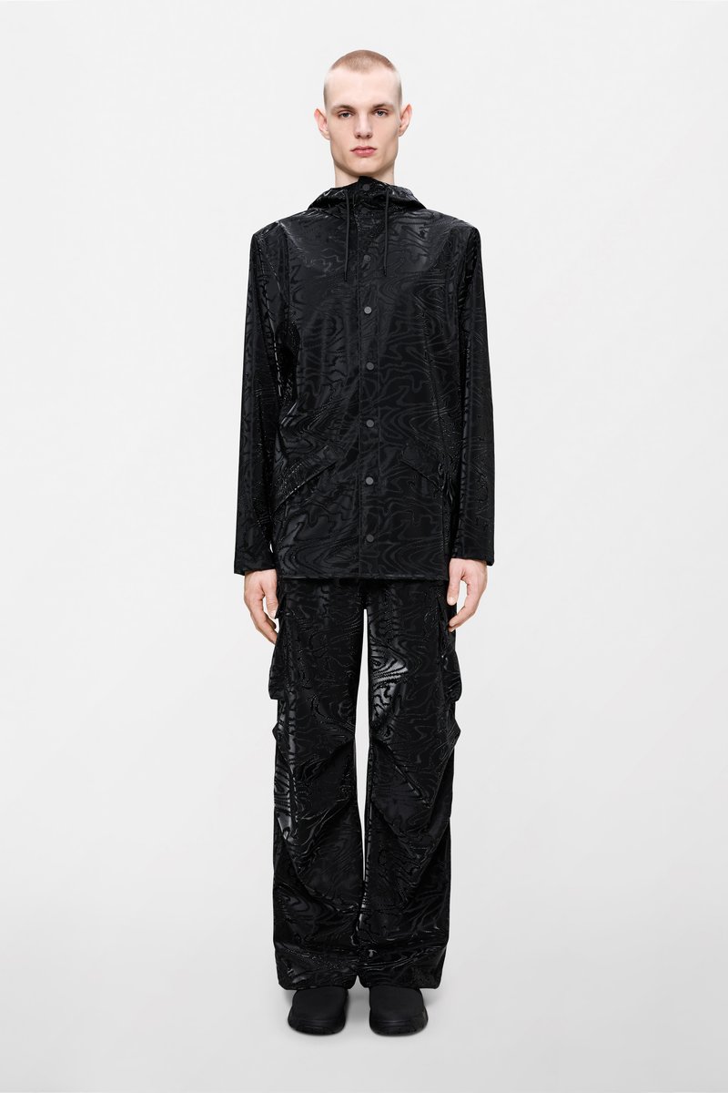 Μαύρο αδιάβροχο μπουφάν με υφή σχεδίασης, συνδυασμένο με χαλαρά παντελόνια σε ταιριαστό σχέδιο. Διαθέτει κουκούλα και κούμπωμα με κουμπιά.