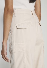 Beiga cargo byxor med en avslappnad passform, som har sidfickor och en texturerad tyg. Designen inkluderar hög midja och detaljer i utilitetsstil.