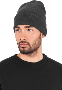 Man with short beard wearing a dark gray knit beanie and black crew neck shirt looking to the side against a white background.