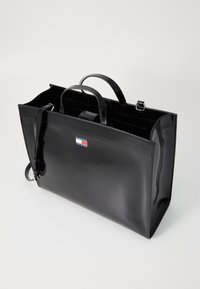 Schwarze Lackleder-Shopper-Tasche mit zwei oberen Griffen, verstellbarem Schultergurt und Tommy Hilfiger Logo-Patch auf der Vorderseite.