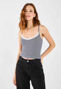 Prúžkovaný crop top v námorníckej modrej a bielej farbe, s čipkovým lemovaním okolo výstrihu, skombinovaný s čiernymi džínsy s vysokým pásom. Ramienka na spaghetti.