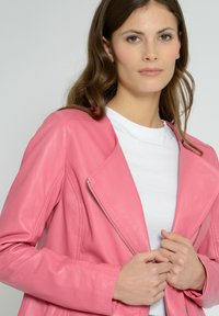 Lyserød læderbikerjakke med en klippet krave, asymmetrisk lynlås og tætsiddende ærmer. Bæres over en hvid t-shirt. Glat tekstur.