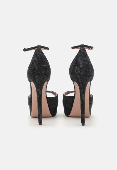 Mustat korkokengät, joissa on teksturoitu kangasvarsi, suippokärki ja nilkkahihna. Varusteena on stiletto-korko ja alustapohja.