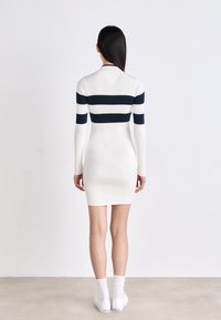 Abito in maglia con maniche lunghe, base bianca con righe orizzontali blu navy, texture a costine e silhouette aderente, abbinato a sneakers bianche.