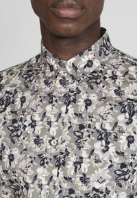 Kwiatowa koszula z guzikami w odcieniu szarym, z białymi i granatowymi kwiatami, z klasycznym kołnierzykiem i dwoma guzikami z przodu. Miękka, lekka tkanina.
