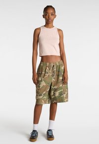 Roze cropped tanktop met het Vans-logo, gecombineerd met knielange camouflage shorts in beige en groen. Schoenen: blauw-grijs met bruine zolen en witte sokken.