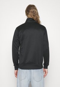 Svart sweatshirt med jämn textur, dragkedja vid halsen, ribbade muddar och fåll. Stylad med ljusblå jeans för kontrast.