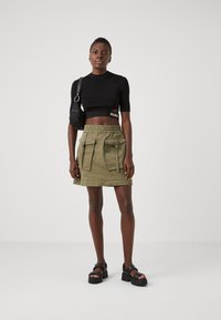 Fekete, cropped top "HUGO" felirattal, olíva zöld szoknya cargo zsebekkel és húzózsinóros derékkal, fekete platform szandál.