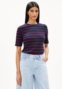 Marineblaues T-Shirt mit roten horizontalen Streifen, Rundhalsausschnitt, kurzen Ärmeln, kombiniert mit hochgeschnittenen hellblauen Jeans.