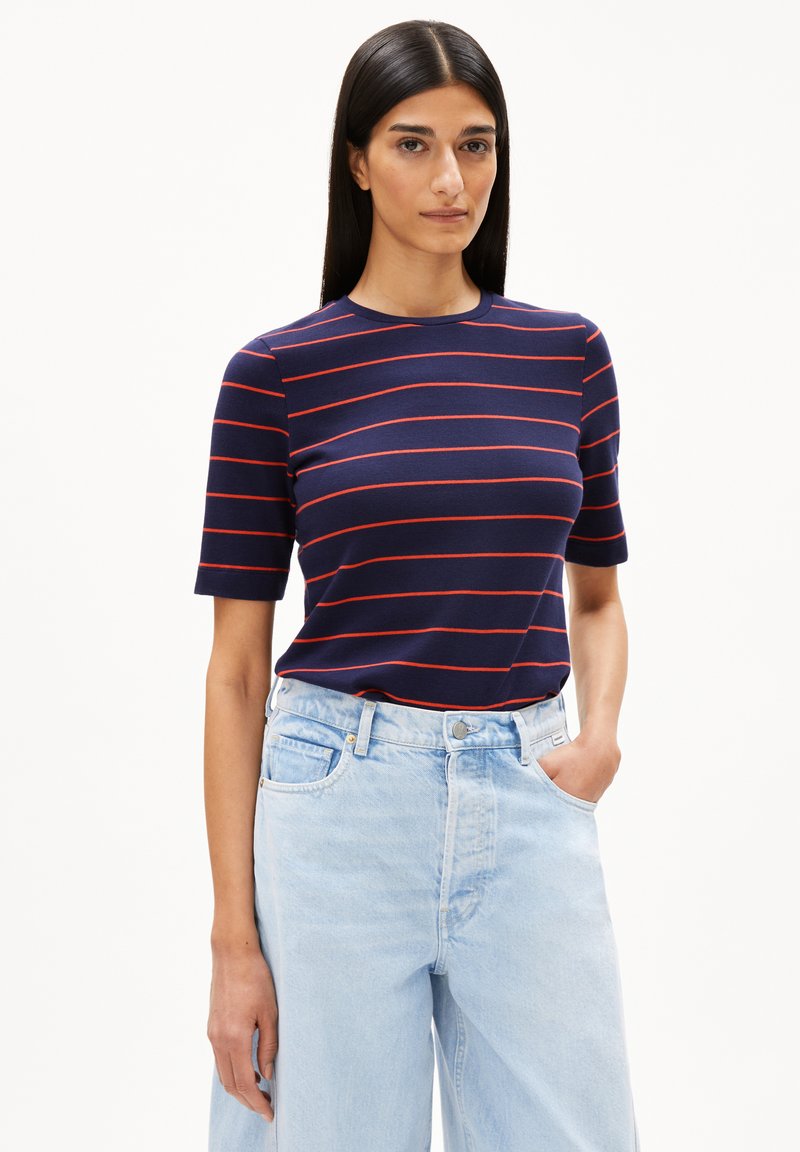 Marineblaues T-Shirt mit roten horizontalen Streifen, Rundhalsausschnitt, kurzen Ärmeln, kombiniert mit hochgeschnittenen hellblauen Jeans.