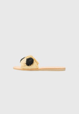 Chinelo plano com parte superior em tecido amarelo, apresentando detalhes florais em conta de pérola pretas, e uma sola de madeira natural. Detalhe de superfície texturizada.