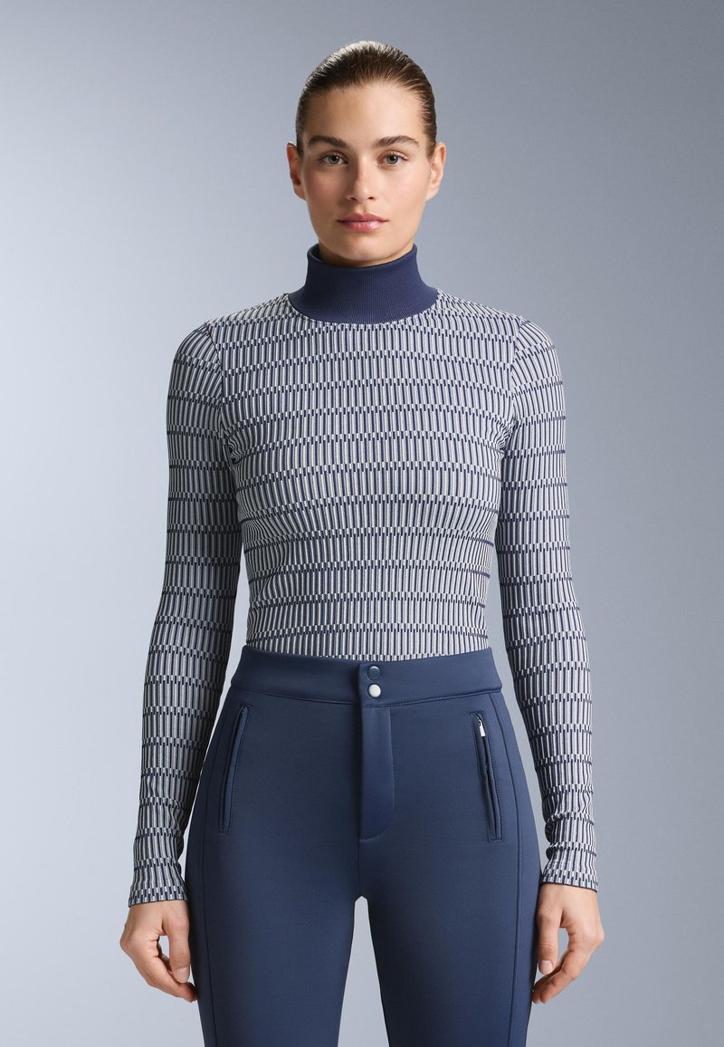 Långärmad topp med hög hals, med ett geometriskt mönster i marinblått och vitt; kombinerad med tajta mörkblå byxor med blixtlås på sidan.