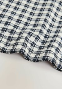 Tessuto a quadri navy e bianco con una texture morbida, caratterizzato da linee intersecate in un motivo a scacchi e un bordo ondulato.
