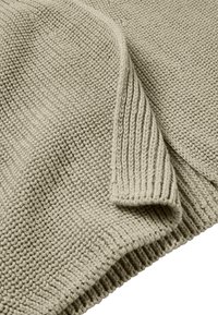 Suéter de punto en beige claro, con una superficie texturizada y puños y dobladillo acanalados, que presenta un patrón de puntos uniforme en toda la prenda.