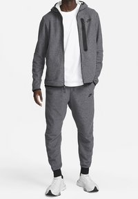 Gray athletic tracksuit featuring a zip-up hoodie with a black zipper pocket and matching joggers. Made of textured fabric, paired with white sneakers.