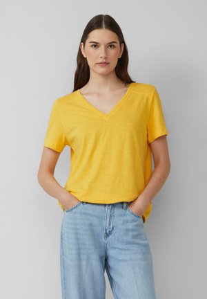 T-shirt jaune à manches courtes et col en V, avec une coupe décontractée, fabriqué en tissu léger. Associé à un jean taille haute bleu clair.