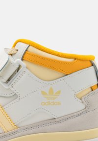 White and yellow mid-top sneaker featuring leather and suede materials, textured accents, and a subtle logo on the side.