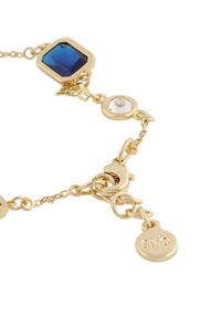 Armband i guldton med en blå åttkantig sten, en klar rund sten och en rund charm med gravyr; länkad kedjedesign.