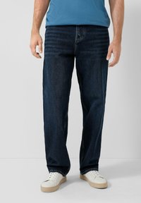 Niebieskie jeansy z ciemnym praniem o prostych nogawkach, z przeszyciami i kieszeniami, zestawione z białymi trampkami.